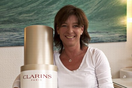 Bild zeigt Silke Bach von Kosmetik und Fusspflege Silke Bach sitzend auf der Kosmetikliege der Firma Gharieni mit einem Werbeprodukt der Kosmetikreihe von Firma Clarins.